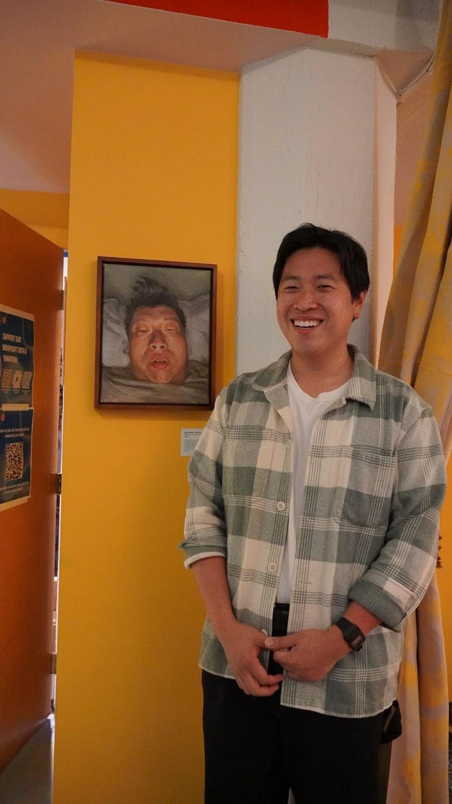 A man poses in front of a vibrant painting featuring a smiling face, showcasing his appreciation for the art.
